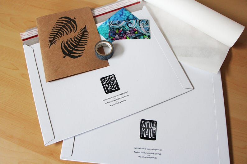 An example of packaging material. Durable cardboard stay-flat mailers have the artists logo stamp displayed as well as social media and website contact information. A card, tape and packing material lays flat on a table display.