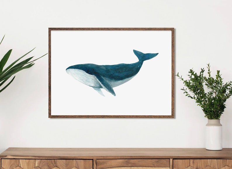 A watercolour print of a humpback whale in shades of blue. A large poster-sized print framed in natural wood in a modern living setting