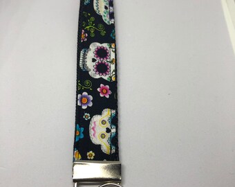 May include: Black and white key chain with a colorful sugar skull design. The key chain has a silver metal ring and a silver metal clasp.