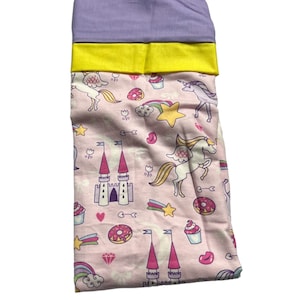 May include: Pink fabric with a unicorn, castle, rainbow, star, cupcake, and donut pattern. The fabric has a purple and yellow border.