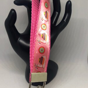 May include: Pink key chain with a white and pink llama pattern. The key chain has a silver metal ring and a silver metal clasp.