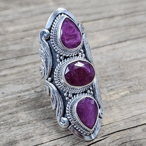 Könnte beinhalten: Ein silberner Ring mit drei violetten Edelsteinen, die in einem detaillierten Design gefasst sind. Der Ring ist ein Statement-Piece mit einem einzigartigen und auffälligen Design.