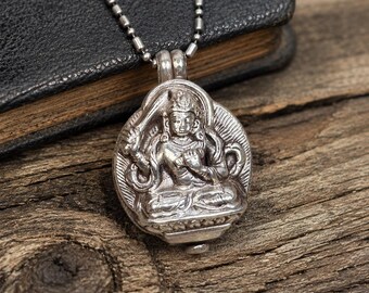 May include: A silver-toned metal pendant featuring a detailed relief of a seated deity with multiple arms, suspended from a matching ball-style chain. The pendant has an oval shape with a textured border and a small loop at the top for the chain.