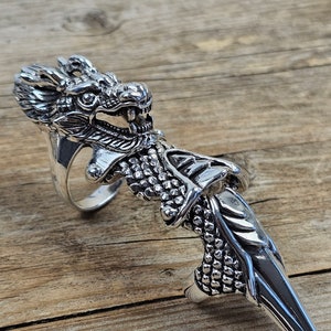 May include: A silver dragon knuckle ring with a detailed design. The ring is made of metal and has a sharp, pointed claw.