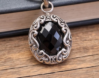 May include: A silver-toned pendant necklace featuring an oval-shaped, faceted black stone set within an ornate, swirling metal frame. The pendant hangs from a smooth, round snake chain, creating a cohesive piece of jewelry with a polished finish.