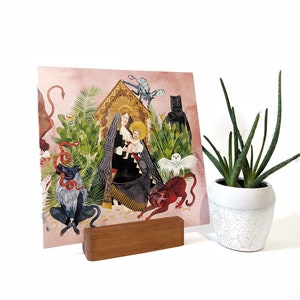 May include: A pink and white record stand with a wooden record holder. The record cover features a colorful illustration of a woman holding a child, surrounded by animals and plants. The record cover has the text "Shroom Queens".