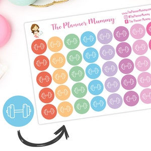 Puede incluir: Una hoja de pegatinas redondas de colores con un contorno blanco de una mancuerna en cada pegatina. Las pegatinas están dispuestas en filas de seis, con cada fila presentando un color diferente: rojo, naranja, amarillo, verde, azul y morado. La hoja está etiquetada como "The Planner Mummy" en la parte superior.