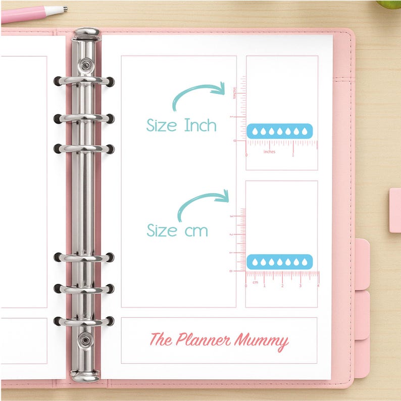 May include: Pink planner with silver binder rings, open to a page with size comparison charts in inches and centimeters. The text "Size Inch" and "Size cm" are displayed. The bottom of the page reads "The Planner Mummy". A pink pen is visible.