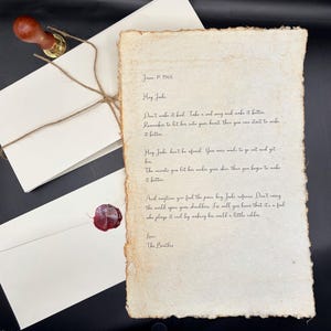 Op de afbeelding: Een handgeschreven brief op verouderd papier, verzegeld met rode was en een houten stempel. De brief wordt vergezeld door twee witte enveloppen, vastgebonden met touw. De tekst bevat "Hey Jude" en is ondertekend met "The Beatles".