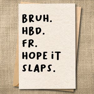 May include: A greeting card with the words "BRUH. HBD. FR. HOPE IT SLAPS." printed in black on a cream-colored card. The card is inside a brown envelope, set against a textured, tan background.
