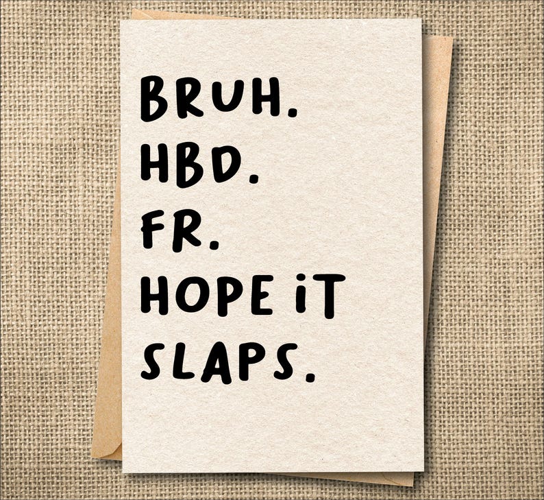 May include: A greeting card with the words "BRUH. HBD. FR. HOPE IT SLAPS." printed in black on a cream-colored card. The card is inside a brown envelope, set against a textured, tan background.