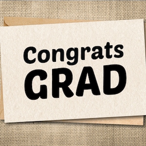 Peut inclure: Une carte de f&eacute;licitations de fin d'&eacute;tudes avec les mots "Congrats GRAD" en lettres noires en gras. La carte est beige clair et repose sur une enveloppe marron. Le fond est un tissu textur&eacute;, beige.