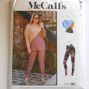 May include: McCall's sewing pattern number 3244 for sizes 18W-20W-22W-24W. The pattern includes instructions for making a hooded top, a short-sleeved top, and leggings. The model is wearing the hooded top and leggings in a brown and pink color scheme.