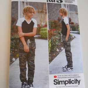 May include: A sewing pattern for a boy's outfit, featuring a black and white striped shirt and camouflage pants. The pattern is from the Simplicity brand and includes instructions for sewing along with Mimi G. The pattern number is S9561.