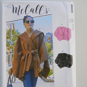 May include: McCall's sewing pattern M8029 for sizes Z (L-XL) featuring three different styles of capes. The first cape is brown and has a tie belt. The second cape is pink and the third cape is black and white plaid. The pattern includes simple instructions. #OdeliaMcCalls