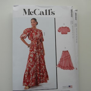 May include: McCall's sewing pattern M8482 for a top and skirt. The pattern includes multiple view options with simple instructions. The model is wearing a red and white floral print top and skirt. The pattern also includes a pink ruffled skirt.