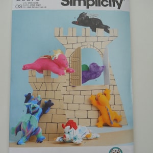 May include: Simplicity sewing pattern S9876 for making five plush dragon toys. The pattern includes instructions for making a black dragon, a pink dragon, a purple dragon, a blue dragon, and a multi-colored dragon. The pattern is designed and printed in the USA.