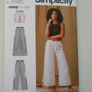 May include: Simplicity sewing pattern number S9956 for pants. The pattern includes three different styles of pants: wide-leg pants with a tie waist, wide-leg pants with a tie waist and cargo pockets, and cropped pants with a tie waist. The pattern is for sizes XS-XXL.