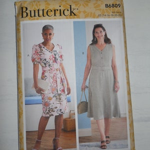 May include: A sewing pattern for two dresses, one with short sleeves and a floral print, and the other sleeveless with a solid light brown color. Both dresses have a V-neckline and a belt. The pattern is from Butterick and is for sizes 14-22.