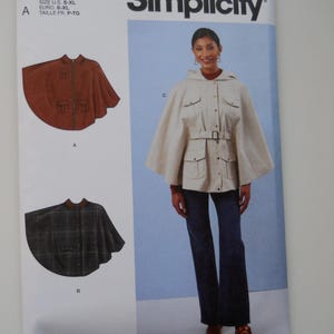 May include: Simplicity sewing pattern S3033 for a hooded cape with pockets and a belt. The pattern includes three different styles: a brown cape, a plaid cape, and a white cape. The pattern is designed for sizes S-XL.