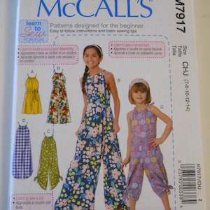 May include: McCall's sewing pattern M7917 for children's clothing sizes 7-8, 10-12, and 14. The pattern includes instructions for making a jumpsuit with a curved hem, a casing and drawstring, and a slit. The pattern is illustrated with four different versions of the jumpsuit, including a floral print, a gingham print, a solid yellow, and a solid green.