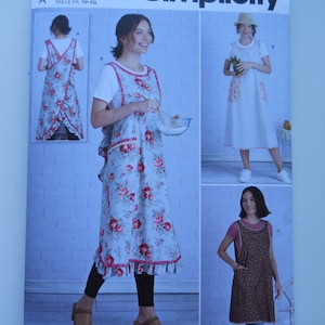 May include: Simplicity sewing pattern S9312. The pattern features three apron designs. One apron is light blue with a red floral print and ruffled edges. The other two aprons are solid white and brown with a small dot pattern.