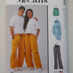 May include: McCall's sewing pattern M8458 for unisex pants. The pattern includes three different views: a green pair of pants, a blue pair of pants, and a gray pair of pants. The pattern is designed and printed in the USA.
