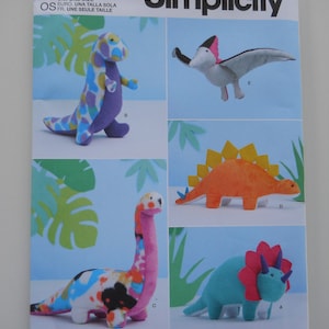 May include: A Simplicity sewing pattern for making five dinosaur plush toys. The pattern includes a triceratops, a pterodactyl, a stegosaurus, a brachiosaurus, and a generic dinosaur. The pattern is labeled "S9585" and "easy-to-sew".
