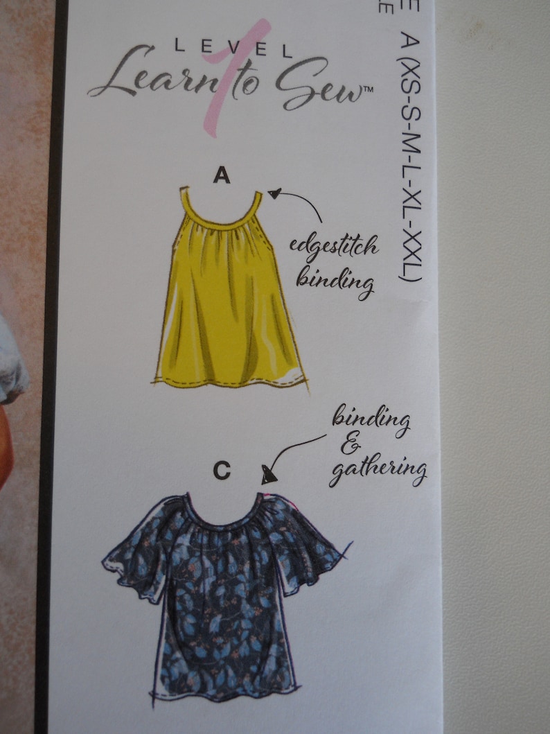 May include: A sewing pattern guide with illustrations of two tops. The first top is yellow and has an edgestitch binding. The second top is blue and white with a floral print and has binding and gathering.