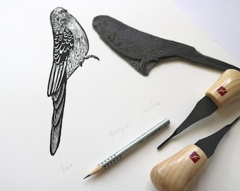 May include: A black and white line drawing of a bird, a wood carving of a bird, two carving tools with wooden handles, and a pencil on a white surface. The text "Budgie" and "Cockatiel" are written on the surface.