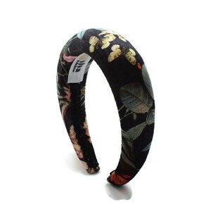 May include: Black headband with a floral print featuring butterflies and leaves. The headband is made of fabric and has a padded design. The brand name "Viva" is printed on the headband.