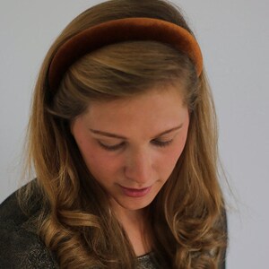 May include: A woman with long brown hair is wearing a brown velvet headband. She is wearing a sparkly gold top.