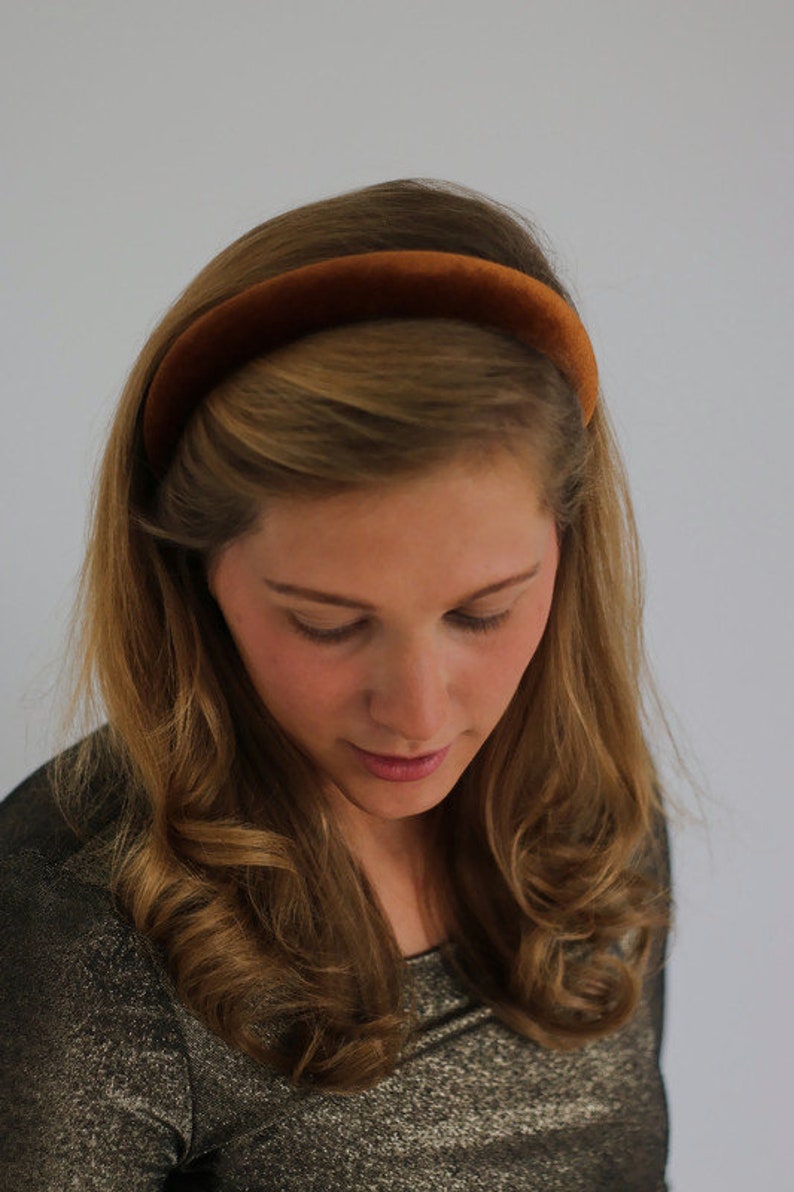 May include: A woman with long brown hair is wearing a brown velvet headband. She is wearing a sparkly gold top.