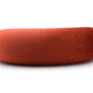 Puede incluir: Una diadema ancha y redondeada hecha de un tejido suave y aterciopelado de color terracota.