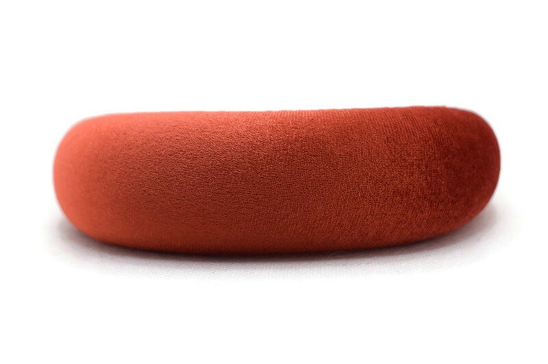 Puede incluir: Una diadema ancha y redondeada hecha de un tejido suave y aterciopelado de color terracota.