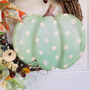 May include: A green and white polka dot pumpkin wreath with a brown stem. The wreath is made of grapevine and has a variety of fall foliage, including leaves, berries, and pine cones.