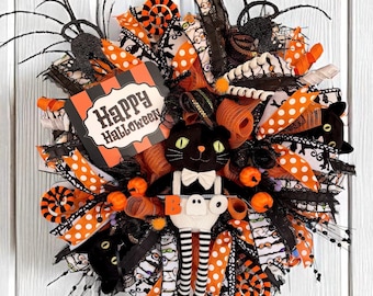 May include: A Halloween wreath with a black cat, orange and white polka dot ribbons, and a sign that says "Happy Halloween." The wreath is decorated with small pumpkins and spider accents.