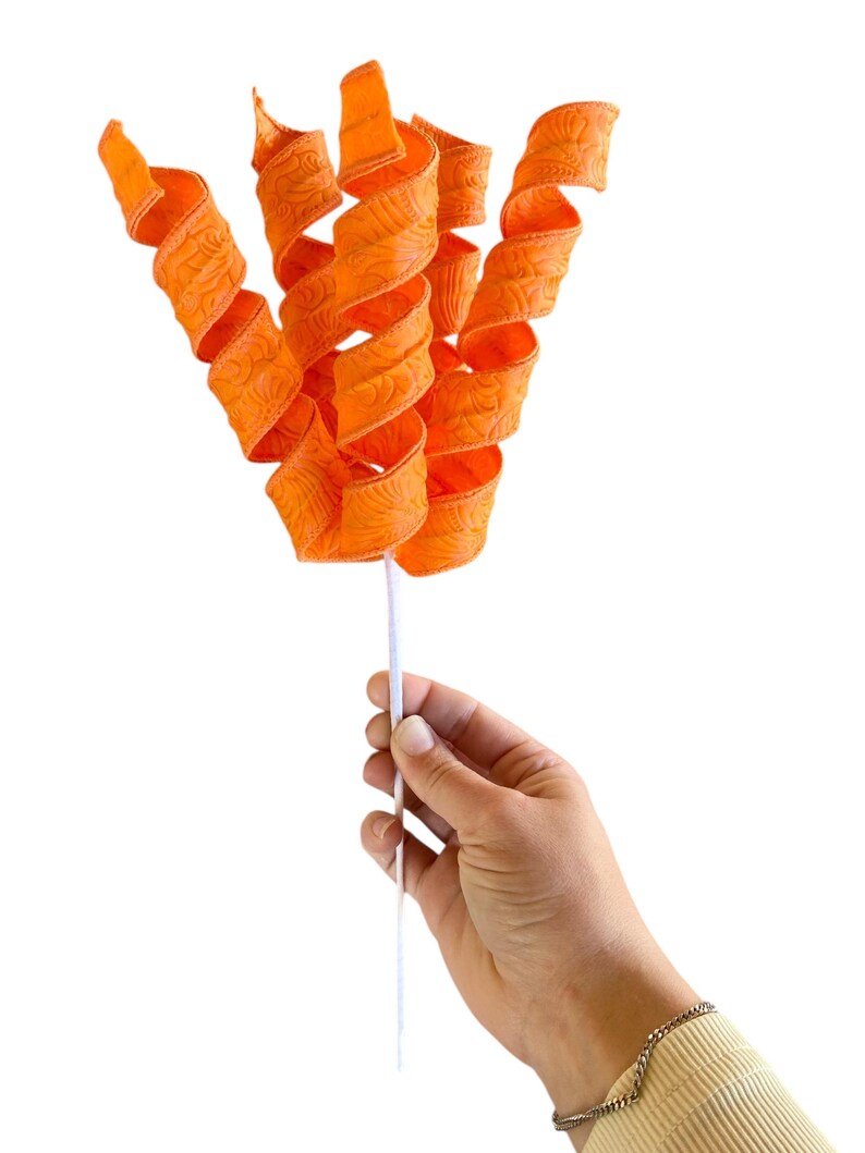May include: A bunch of orange curly ribbon with a white stem. The ribbon has a textured pattern.
