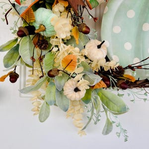 May include: A green and white polka dot pumpkin wreath with a brown ribbon, green and white pumpkins, and fall foliage.