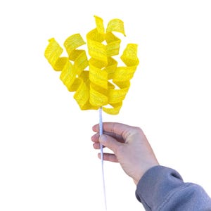 May include: A yellow paper streamer with a swirl design, held by a hand on a white background.