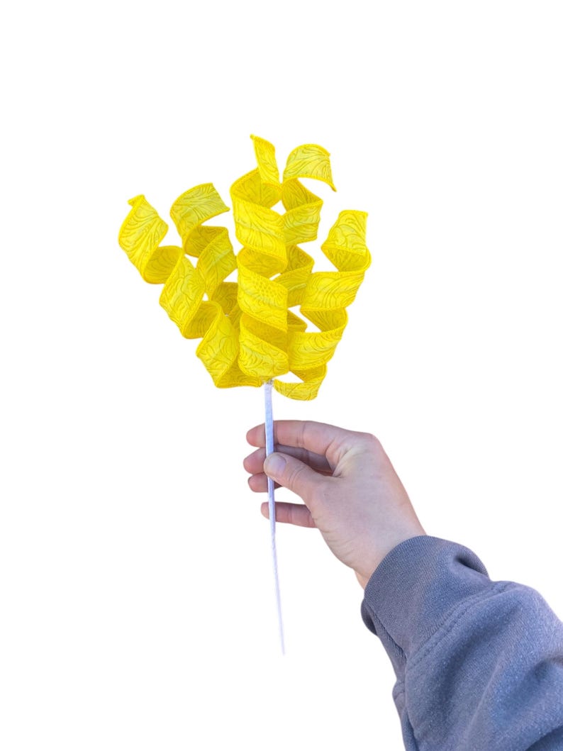 May include: A yellow paper streamer with a swirl design, held by a hand on a white background.