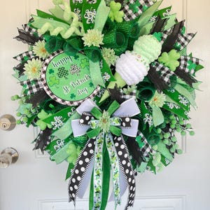 May include: A green, black, and white St. Patrick's Day wreath with a green and white shamrock ice cream cone, a black and white checkered ribbon, and a sign that says "Happy St. Patrick's Day".
