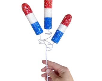 May include: Three red, white, and blue firework-shaped decorations on a white wire stem.