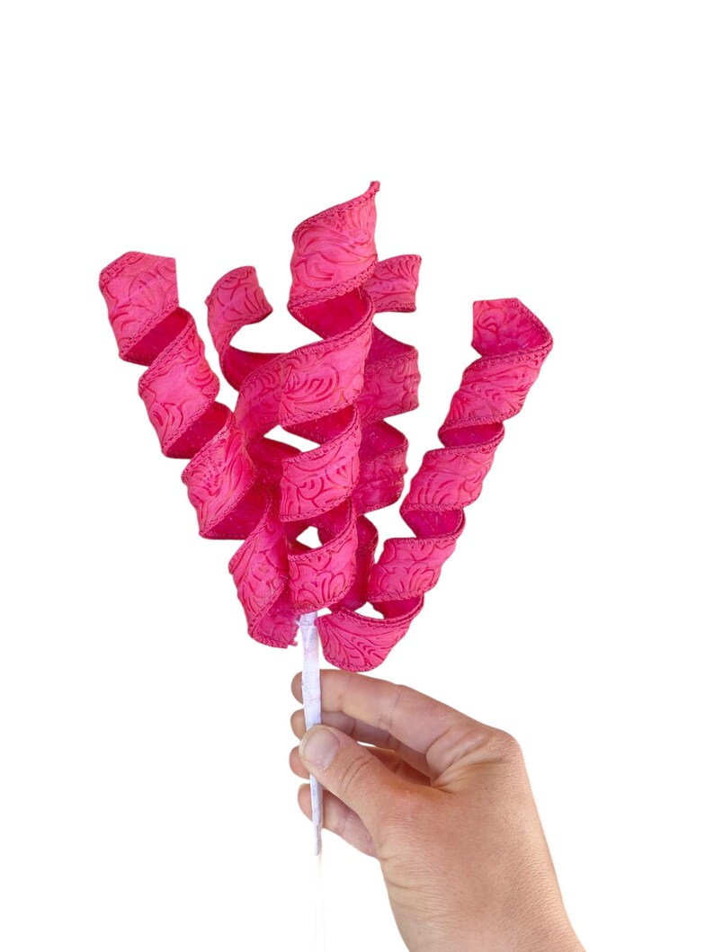 May include: A pink curly ribbon with a white stem. The ribbon has a floral pattern and is curled into a spiral shape.
