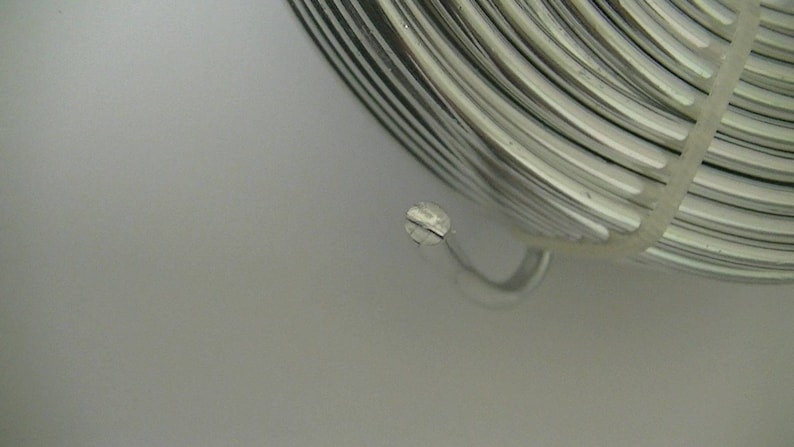 Op de afbeelding: Een rol zilverkleurige draad met een witte plastic spoel. De draad is opgerold en heeft een glanzende afwerking.