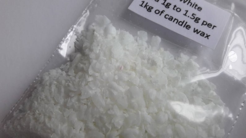 May include: White candle wax flakes in a clear plastic bag. The bag has a label that reads "White 1g to 1.5g per 1kg of candle wax".