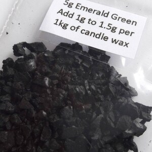 May include: A small plastic bag filled with dark green emerald green candle dye flakes. The bag has a label that reads "5g Emerald Green Add 1g to 1.5g per 1kg of candle wax".