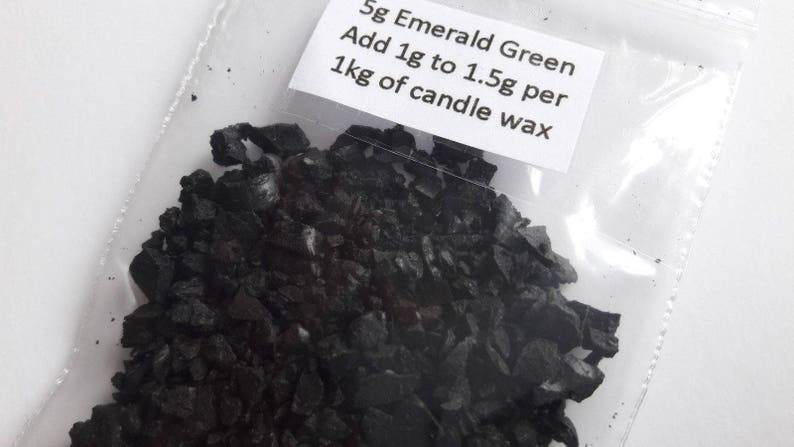 May include: A small plastic bag filled with dark green emerald green candle dye flakes. The bag has a label that reads "5g Emerald Green Add 1g to 1.5g per 1kg of candle wax".