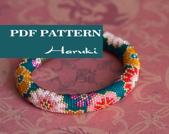 May include: A beaded bracelet with a floral pattern in shades of pink, red, yellow, and teal. The bracelet has the text "PDF PATTERN" and the name "Haruki" in white. The background is a pink floral pattern.