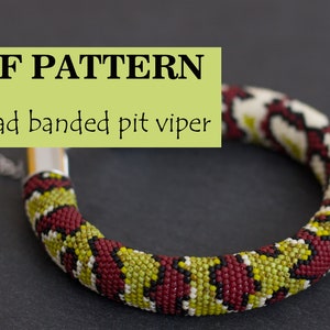 以下が含まれることがあります： ビーズでできたヘビのブレスレットのPDFパターン。ブレスレットは赤、緑、黒、白です。グレーの表面に置かれたブレスレットのクローズアップです。
